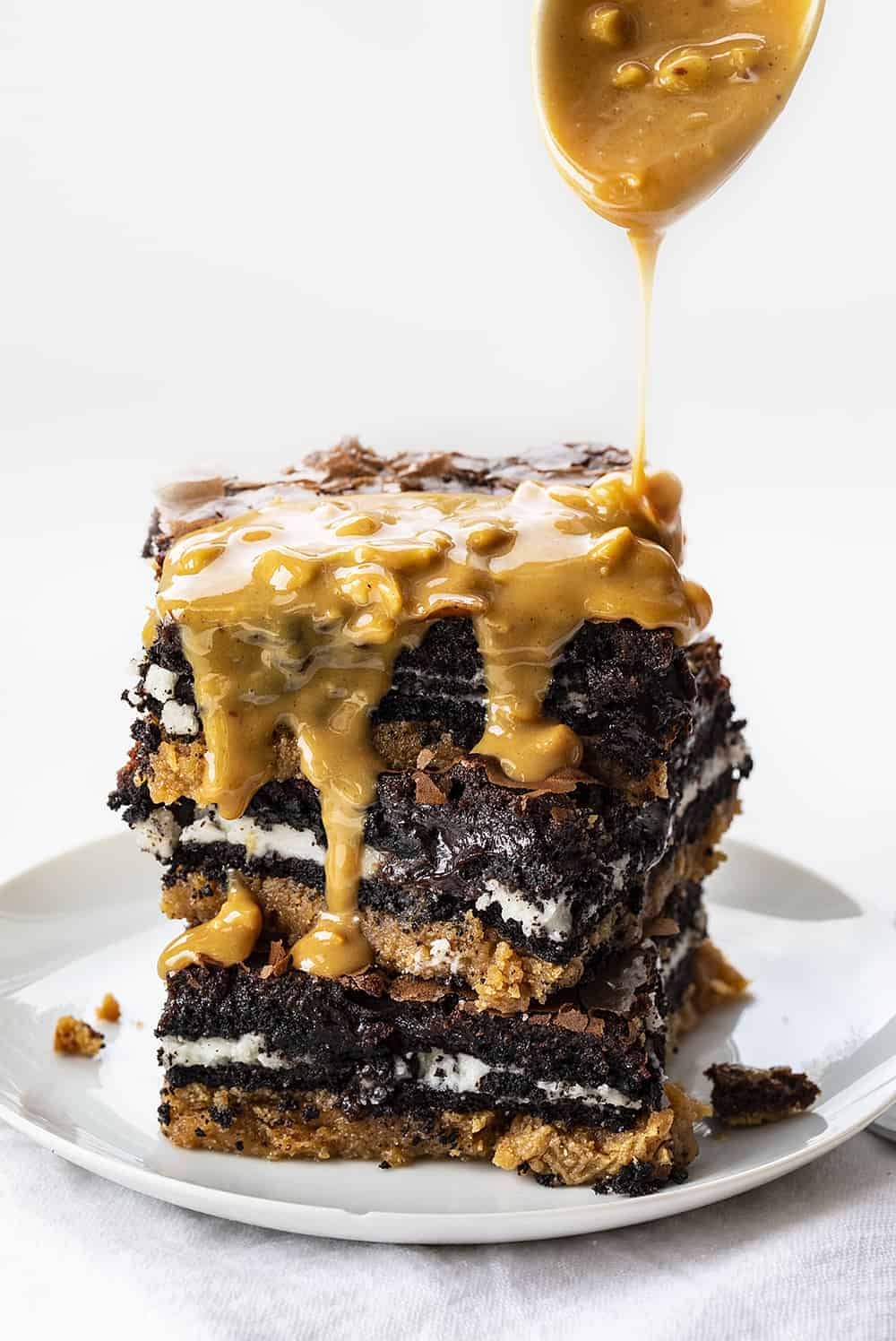 Peanut Butter Slutty Brownies are a decadent dessert that starts with a layer of a peanut butter cookie, followed by a layer of double-stuffed Oreo cookies and topped with chocolate brownie! Slutty Brownies, Oreo Brownies. Peanut Butter Slutty Brownies, How to Make Slutty Brownies, Variations of Slutty Brownies, Easy Slutty Brownies. Chocolate Brownies, i am baker, baking, recipes, brownies, iambaker Stack of Peanut Butter Slutty Brownies with Peanut Butter Butterscotch Sauce Being Drizzled Over Top