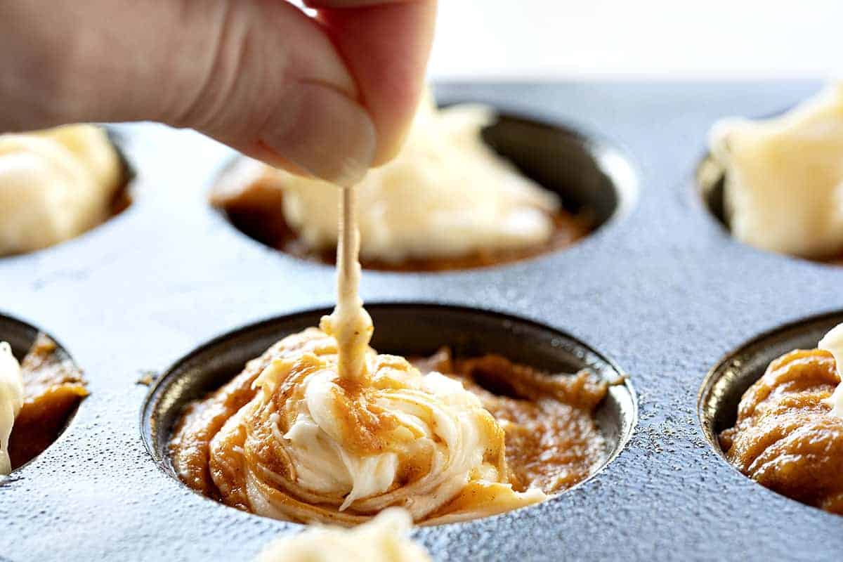 With a cream cheese swirl and a perfectly moist pumpkin muffin, Pumpkin Cream Cheese Swirl Muffins are the best thing about pumpkin spice season! #pumpkincreamcheeseswirlmuffins #muffinrecipes #pumpkinmuffins #iambaker #homemadepumpkinspice #pumpkinspice #baking #desserts #creamcheesefilledmuffins Swirling Cream Cheese in Pumpkin Batter